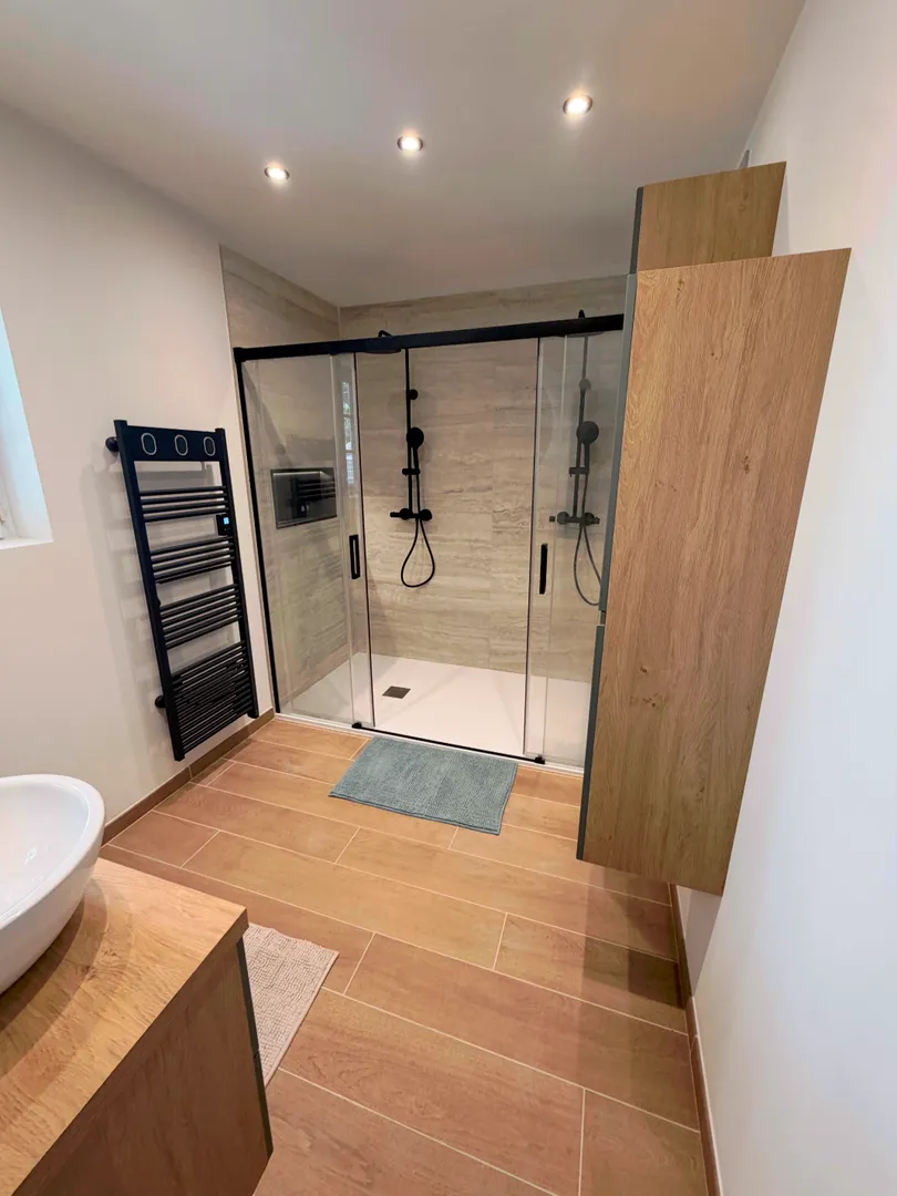 Salle de bain rénovée par Busato Service avec meuble vert, double vasque, plan en bois et grand miroir rond.