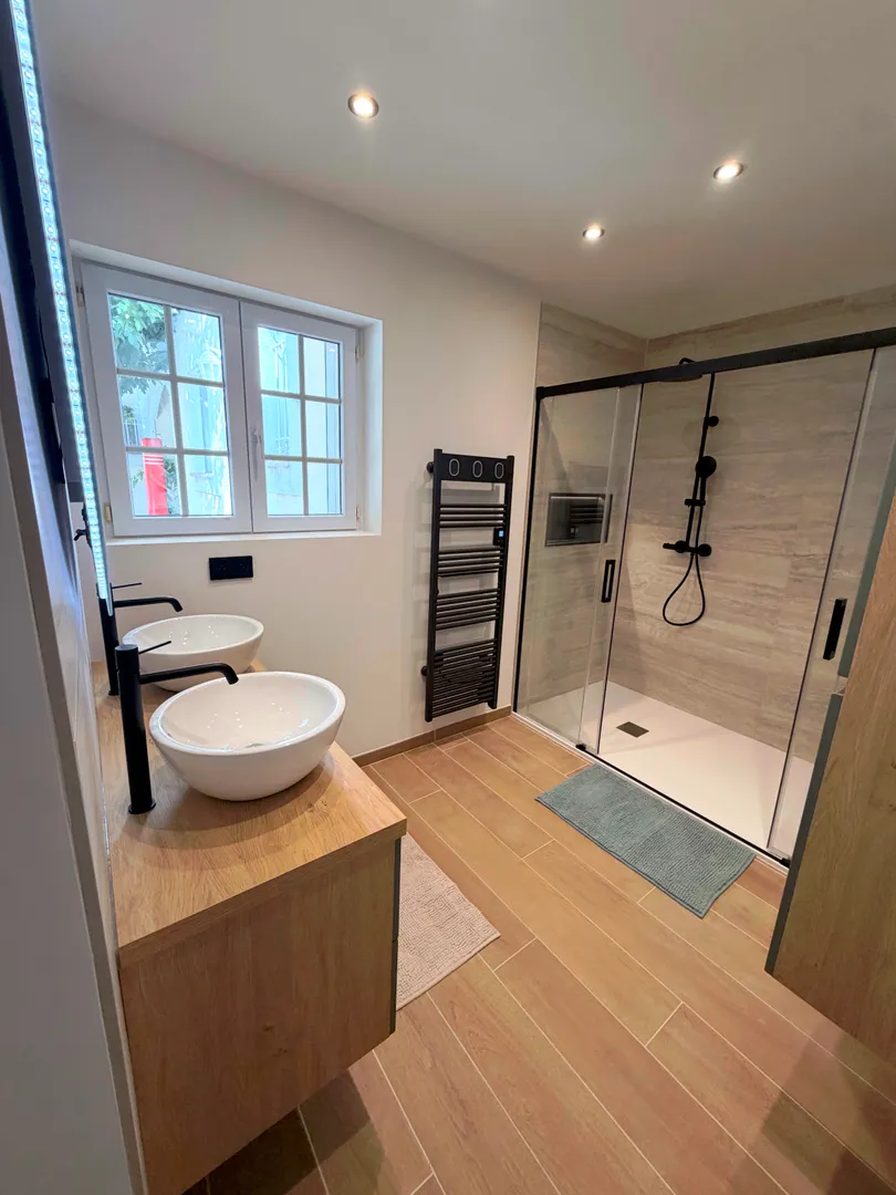 Salle de bain contemporaine avec double douche, paroi vitrée noire et carrelage effet bois, réalisée par Busato Service.