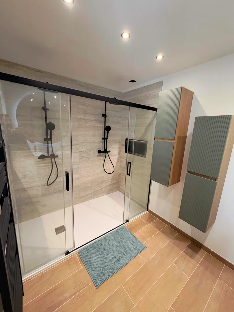 Meuble de salle de bain vert avec deux vasques blanches, robinets noirs et miroir rond pour une ambiance naturelle et moderne.