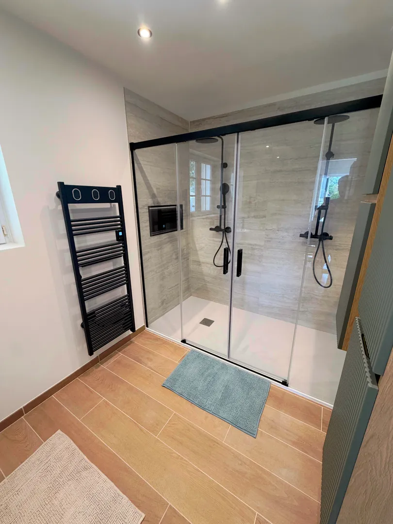 Espace double douche avec niche rétroéclairée, carrelage mural effet pierre et meubles suspendus verts et bois.
